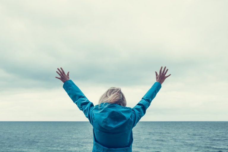 a-rear-view-of-a-single-girl-with-her-arms-raised-high-in-the-air-whilst-facing-the-ocean-in-an-act_t20_OzagRG